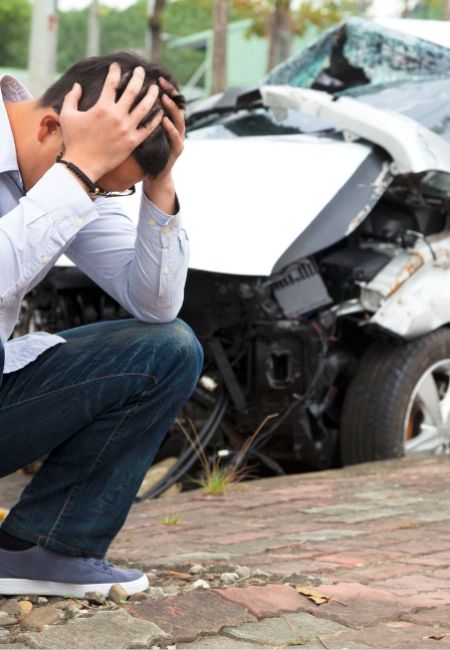 Avvocato Andrea Bottoli: Primo piano di un ragazzo con le mani in testa e allo sfondo la sua macchina distrutta per un incidente stradale.